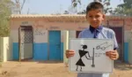 A schoolboy stands in front of a block of toilets holding a hand-drawn poster