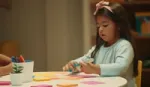 A photograph of a child writing something on a piece of paper.